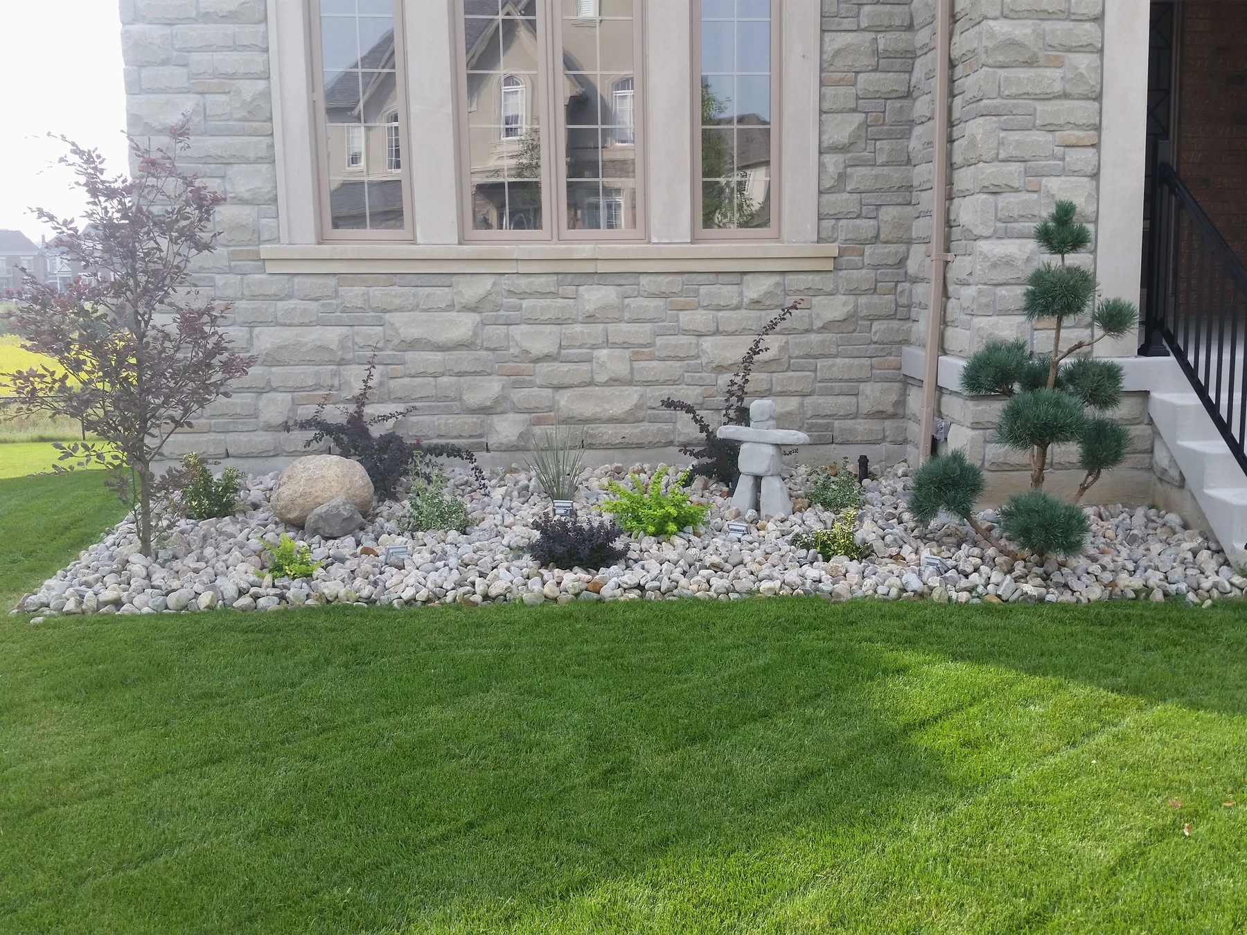 Lawn and stone garden bed beside an established home from the KNPM website archive.