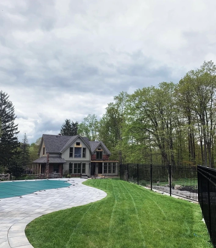 Freshly mown lawn alongside a covered swimming pool, curved paving and black fencing.